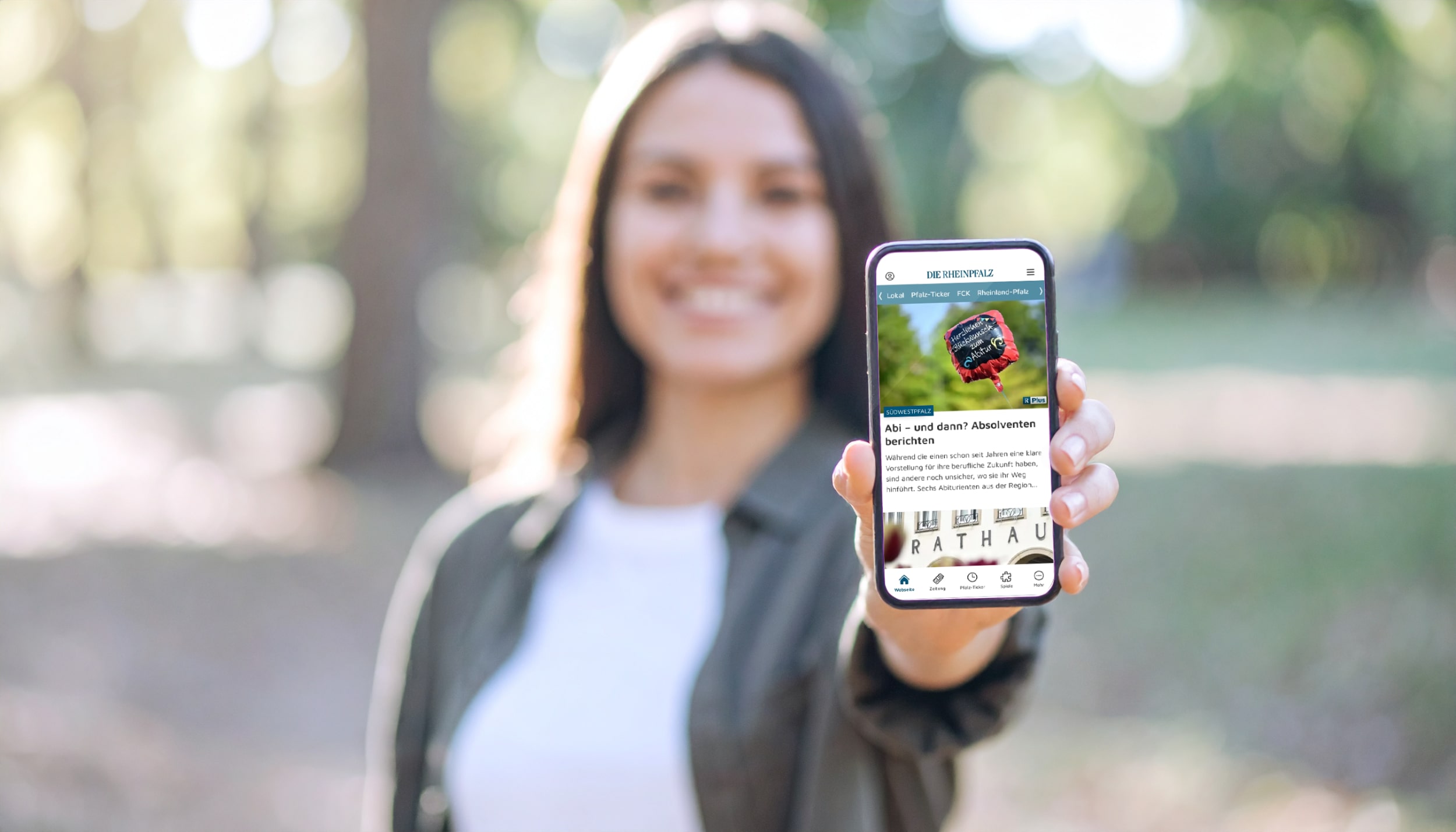 Junge Frau hält lächelnd ein Smartphone mit der geöffneten RHEINPFALZ-App in die Kamera.