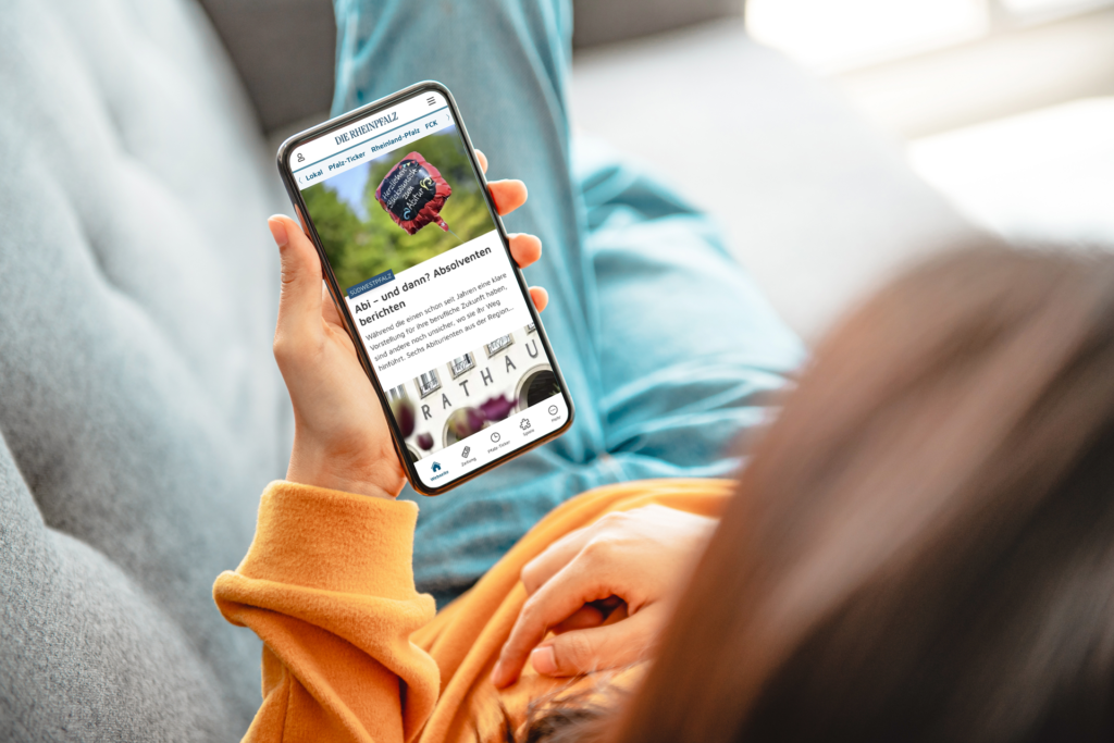 Junge Frau ruft auf ihrem Smartphone die Startseite der RHEINPFALZ App auf