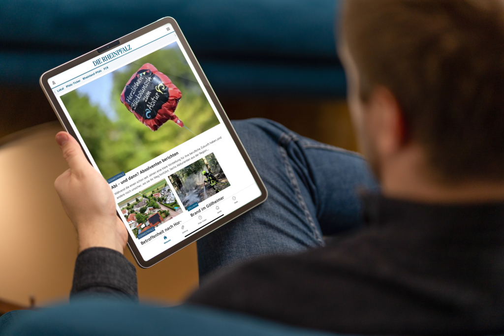 Ein Blick über die Schulter eines jungen Manns; er ruft auf seinem Tablet die Startseite der RHEINPFALZ App auf.